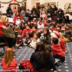 Mayor Pam reading to children on the floor of city hall during the annual Youth Bureau Milk and Cookies holiday event.